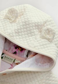 Biely prešívaný kapucňový odev s dvoma malými mašľovými akcentmi; podšitý kvetinovým vzorom. Na štítku je napísané "BAKER by Ted Baker."