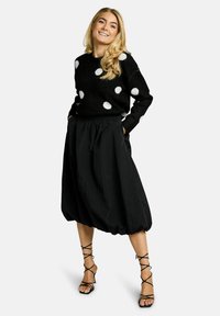 Maglione nero a pois bianchi, abbinato a una gonna nera al ginocchio, ampia e voluminosa. Scarpe con tacco alto nere e con cinturini completano l'outfit.