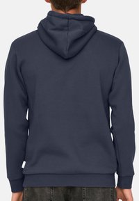 Felpa cappuccio di un blu scuro navy con cordino, maniche lunghe e orlo a coste. Realizzata in tessuto morbido con una texture liscia, presenta un'etichetta sul lato.