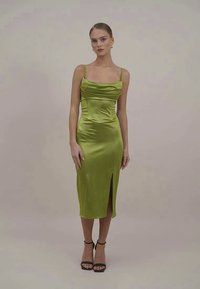 Vestido verde de satin com alças finas, corpete justo e fenda lateral, apresentando um decote drapeado e uma textura suave.