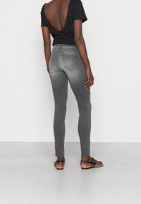 Jeans skinny grises con una cinturilla de altura media y un acabado deslavado. Los bolsillos traseros presentan un detalle con un logo en forma de triángulo. Camisa negra con un escote profundo en la espalda.