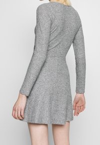 Robe grise à manches longues en tissu tricoté texturé, avec une jupe évasée et un corsage ajusté. La vue arrière montre un col rond et des détails de couture.