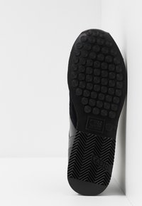 Semelle d'une basket noire avec une empreinte circulaire près des orteils et un motif en zigzag près du talon, marquée "Cruyff" et "Rapid", taille 42.