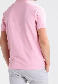 Polo à manches courtes en coton rose clair, avec col, texture subtile et fentes à l'arrière pour faciliter les mouvements.