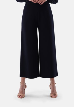 Marine-blaue weite Hose, glatter Stoff, hoch tailliertes Design mit fließender Silhouette, kombiniert mit nacktfarbenen Absatzsandalen mit Knöchelriemen.