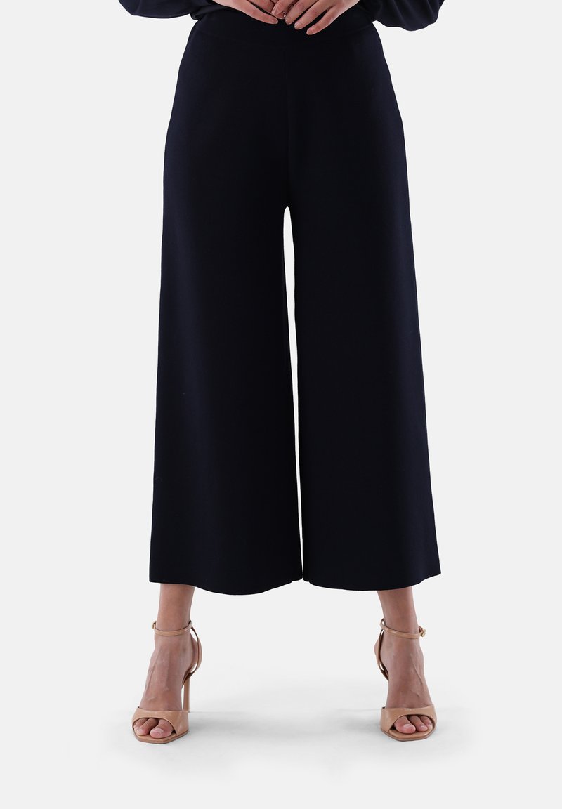 Marine-blaue weite Hose, glatter Stoff, hoch tailliertes Design mit fließender Silhouette, kombiniert mit nacktfarbenen Absatzsandalen mit Knöchelriemen.