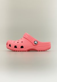 Sabot rose à enfiler avec des trous de ventilation, une bride de talon ajustable, une semelle texturée et un logo circulaire sur la bride, sur un fond uni.