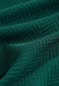 Strukturierter Stoff in tiefem Grün mit einem Fischgrätenmuster, das eine weiche, plüschige Oberfläche und ein gewebtes Design mit erhabenen Akzenten zeigt.