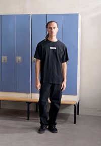 Black t-shirt with "JUVENTUS" logo, paired with black pants and black sneakers, standing in front of blue lockers on a wooden bench.