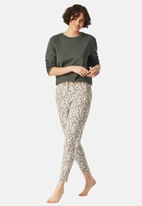 Haut à manches longues vert associé à un pantalon crème à motifs avec des accents floraux en bleu et noir. Le pantalon a une taille à cordon.