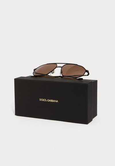 Dolce & Gabbana napszemüveg barna árnyalatú lencsékkel, fekete fémből készült kerettel és állítható orrpárnákkal, egy fekete dobozon bemutatva, arany logóval.