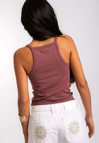 Top sin mangas burdeos con tirantes gruesos, diseño ajustado, combinado con pantalones cortos blancos con girasoles bordados en los bolsillos traseros.