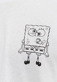Hvid bomulds t-shirt med et sort konturdesign af en tegneseriefigur med store øjne, iført slips, kvadratiske bukser og sko.
