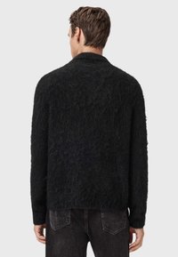 Jersey negro texturizado con un corte holgado, cuello alto y mangas largas, combinado con jeans oscuros.
