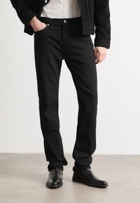 Jeans en denim noir avec une coupe droite, dotés de poches avant, d'une braguette zippée et de accents de bouton métalliques. Texture lisse.