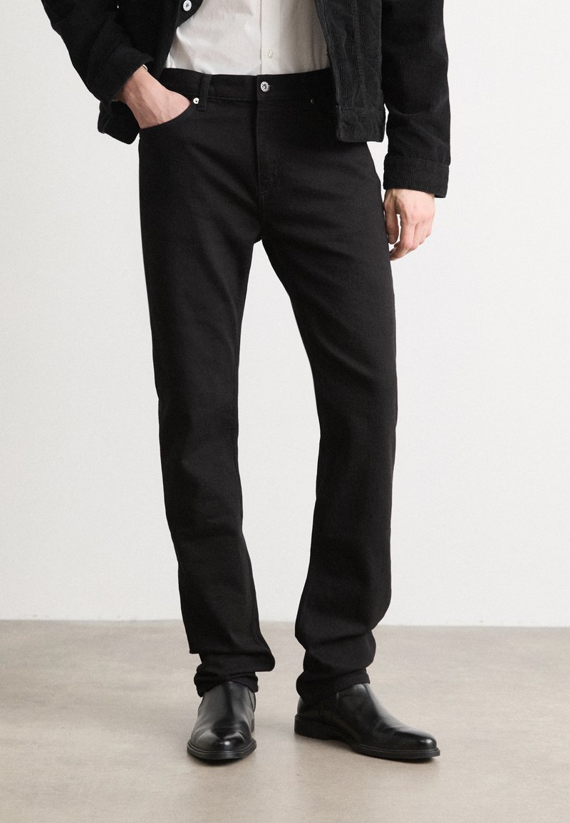Jeans en denim noir avec une coupe droite, dotés de poches avant, d'une braguette zippée et de accents de bouton métalliques. Texture lisse.