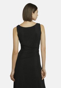 Schwarzes ärmelloses Kleid mit rundem Ausschnitt, eng anliegendem Oberteil und fließendem Rock. Das Material hat einen subtilen Schimmer und weist an der Taille geraffte Details auf.