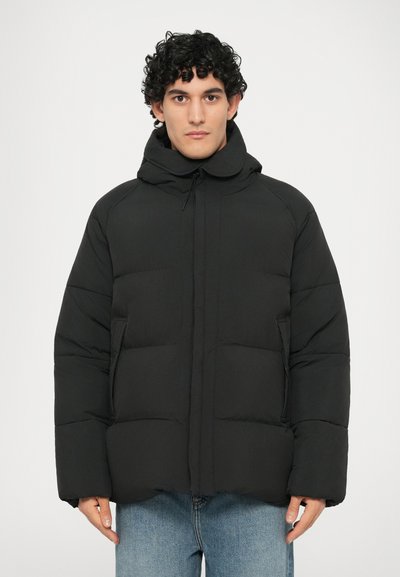 Veste rembourrée noire avec un col montant et une fermeture éclair, dotée de poches avant et d'un design compact pour la chaleur. Texture lisse, motif matelassé.