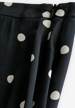 Schwarzer Stoff mit großen cremefarbenen Polka-Dots; glatte Textur, drapierter Schnitt und Reißverschluss oben.
