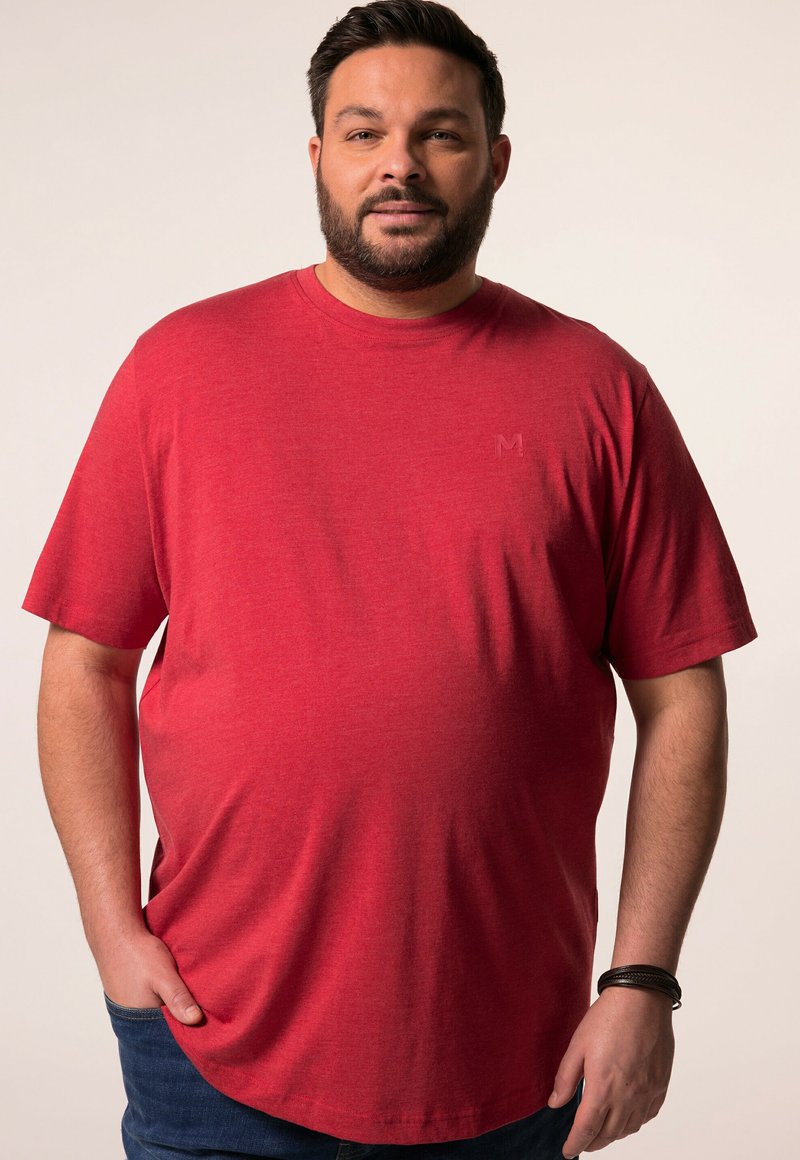 Rotes T-Shirt mit kurzen Ärmeln, feiner Textur und abgerundetem Saum. Mit kleinem, eingeprägtem 'M'-Logo auf der Brust. Getragen mit dunklen Jeans.
