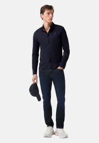 Marineblauwe overhemd met lange mouwen en een slim fit, gecombineerd met donkere spijkerbroeken en witte sneakers, afgewerkt met een marineblauwe pet.