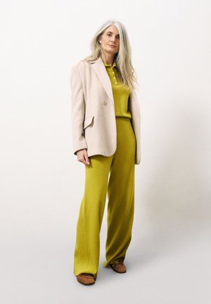 Beige op maat gemaakte blazer over een aansluitende felgroene gebreide top en groene broek met wijde pijpen. Bruine ballerina's maken de outfit compleet.