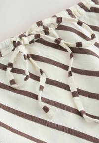 Close-up of white fabric with horizontal brown stripes and a tied drawstring at the waistband, showing texture and stitching details.