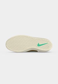 Σόλα μπεζ παπουτσιού Nike με μοτίβο πέλματος και τιρκουάζ λογότυπο Nike κοντά στην περιοχή των δακτύλων σε ανοιχτό γκρι φόντο.