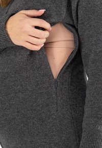 Vêtement en tricot gris avec une ouverture zippée révélant une couche marron clair en dessous. La texture semble douce et confortable, avec des poignets côtelés.
