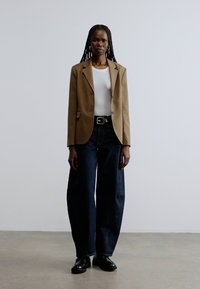 Pruun bleiser valge särgiga, kombineeritud tumelõõtsade siniste laia säärega teksade ja mustade kingadega. Sile bleiseri materjal, kontrastsed tekstuurid.