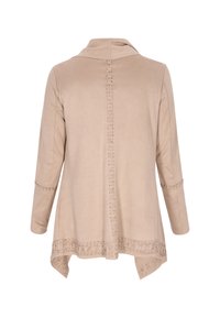 Beige műsuede dzseki hosszú ujjakkal, gallérral és díszítő varrással a háton és a szegélynél. Aszimmetrikus szabás az alján.