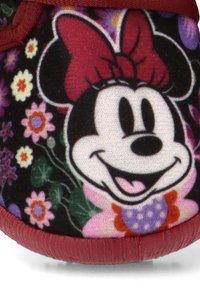 Zapatilla de tela negra con la cara de Minnie Mouse y un lazo rojo, rodeada de patrones florales coloridos y un borde suave y texturizado.
