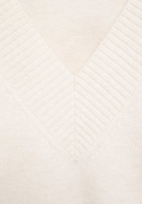 Tissu en maille couleur crème avec un motif côtelé en forme de V le long de l'encolure, montrant une texture douce et des détails de couture raffinés.