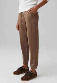 Brown, soft suede pants with a relaxed fit, side pockets, and tapered cuffs, paired with dark brown sneakers with laces.