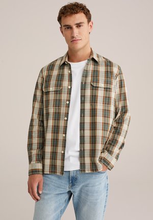 Geruite shirt in groene, beige en bruine tinten, met een doorlopende knoopsluiting, twee borstzakken en lange mouwen, gecombineerd met een witte T-shirt eronder.