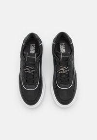 Mustat nahkaiset tennarit, joissa valkoinen pohja, metalliset nauhakenkäkoristeet ja teksturoitu musta kieli. Logot näkyvästi esillä kielen päällä.