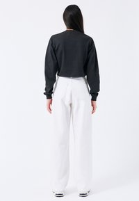 Sudadera negra recortada de manga larga combinada con pantalones de pierna ancha blancos de talle alto. Texturas suaves y diseño minimalista.