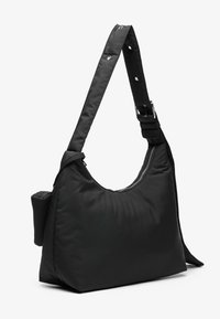 Zwarte nylon schoudertas met een ronde vorm, ritsluiting en verstelbare schouderband. Beschikt over een klein zijvak voor extra opbergruimte.