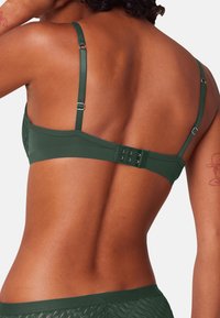 Ciemnozielony stanik z regulowanymi ramiączkami, gładką teksturą oraz zapięciem na haki z tyłu, oferującym trzy opcje zapięcia.