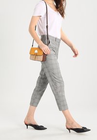 Pantaloni a quadri grigi con un taglio sartoriale, abbinati a una T-shirt bianca a scollo a V e mule nere open-toe. Una piccola borsa multicolore completa l'outfit.