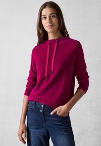 Felpa con cappuccio fucsia realizzata in tessuto texturizzato, con coulisse, maniche lunghe e vestibilità rilassata, abbinata a jeans blu.