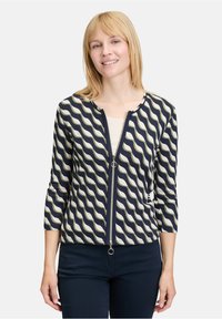 Granatowa kurtka zip z kremowym falistym wzorem, rękawami o długości trzech czwartych, rypsowaną teksturą i srebrnymi akcentami.