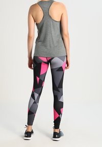 Top de tirantes gris con corte racerback combinado con leggings ajustados que presentan un patrón geométrico en negro, rosa y gris. El material parece elástico.