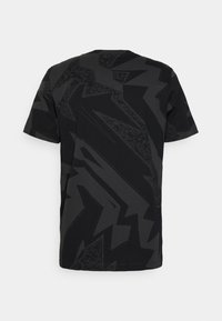 Camiseta negra de manga corta con patrones angulares abstractos en gris oscuro que cubren la parte trasera y las mangas.