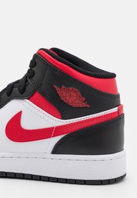 Černá kožená teniska s červenými a bílými akcenty, vysoký střih, viditelné logo Air Jordan a texturovaný povrch. Bílá mezipodešev a černá podrážka.