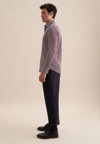 Koszula w kratę z długim rękawem w kolorze fioletowym i białym, w zestawieniu z ciemnymi spodniami i czarnymi butami. Widok z boku, widoczne zapinane mankiety.