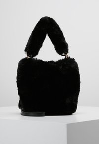 Czarna torebka z sztucznego futra o miękkiej, puszystej teksturze, zaokrąglonym górnym uchwycie i płaskiej podstawie. Złote akcenty metalowe.