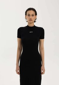 Czarna sukienka o dopasowanej sylwetce, krótkich rękawach, wysokim dekolcie i subtelnym logo na wysokości klatki piersiowej. Gładka tekstura materiału, minimalistyczny design.
