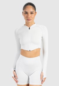 Veste blanche, côtelée, courte avec des manches longues et une fermeture éclair à l'avant. Assortie à un short blanc taille haute avec des découpes sur les côtés.