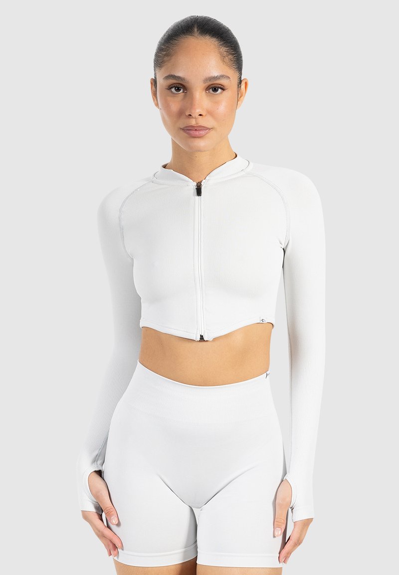 Veste blanche, côtelée, courte avec des manches longues et une fermeture éclair à l'avant. Assortie à un short blanc taille haute avec des découpes sur les côtés.